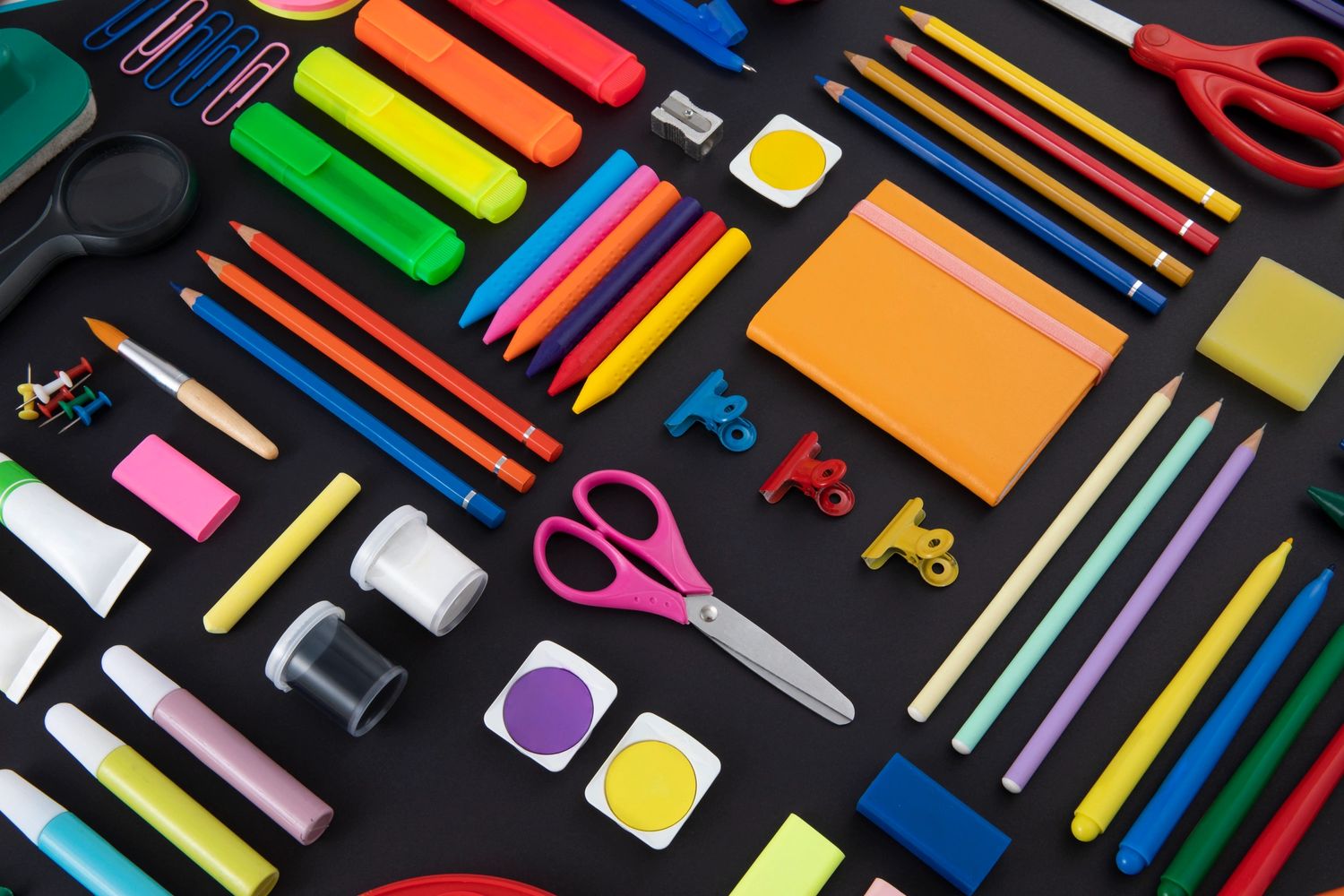 Assortment of colorful stationery items neatly arranged on a black surface.