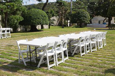 White folding tables and chairs set outdoors on a sunny lawn for an event.
