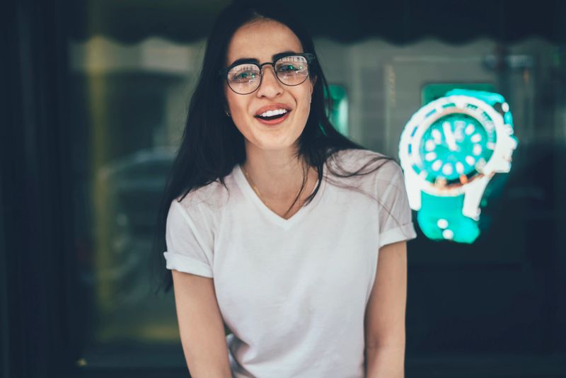 Casual dressed female student in mockup t-shirt with copy space for brand label smiling at camera during leisure, cheerful millennial woman in opticals spectacles for vision correction posing