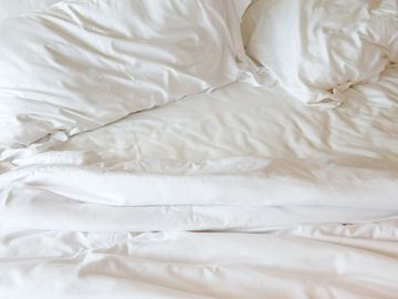 Crumpled white bed sheets and pillows on a bed.
