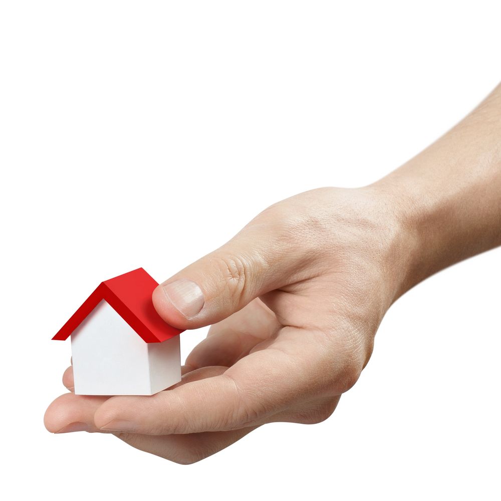 Hand holding a small white house model with a red roof.