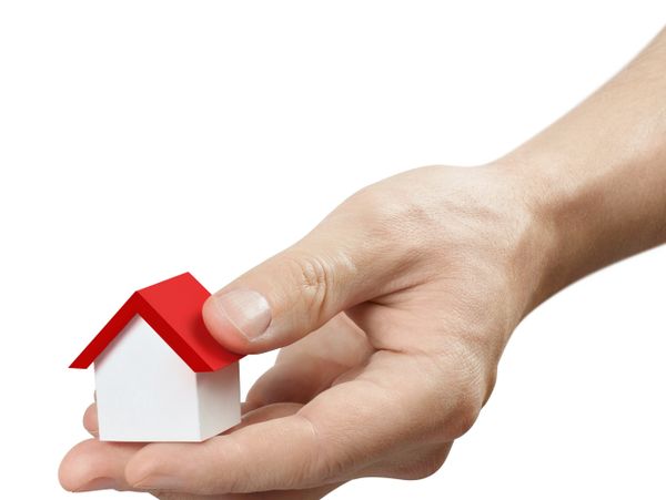 Hand holding a small white house model with a red roof.