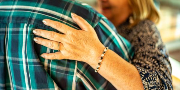 Woman's hand with ring resting on man's shoulder.