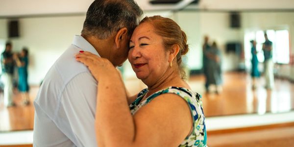 An elderly couple shares a tender dance in a bright room with mirrors.