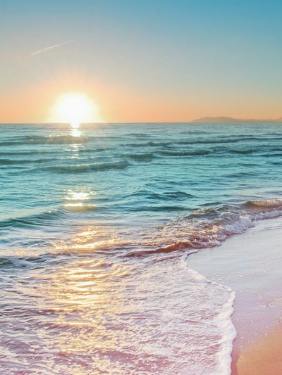 Sunset over a calm ocean with gentle waves washing onto the sandy shore.