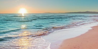 Sun setting over a serene beach with gentle waves.