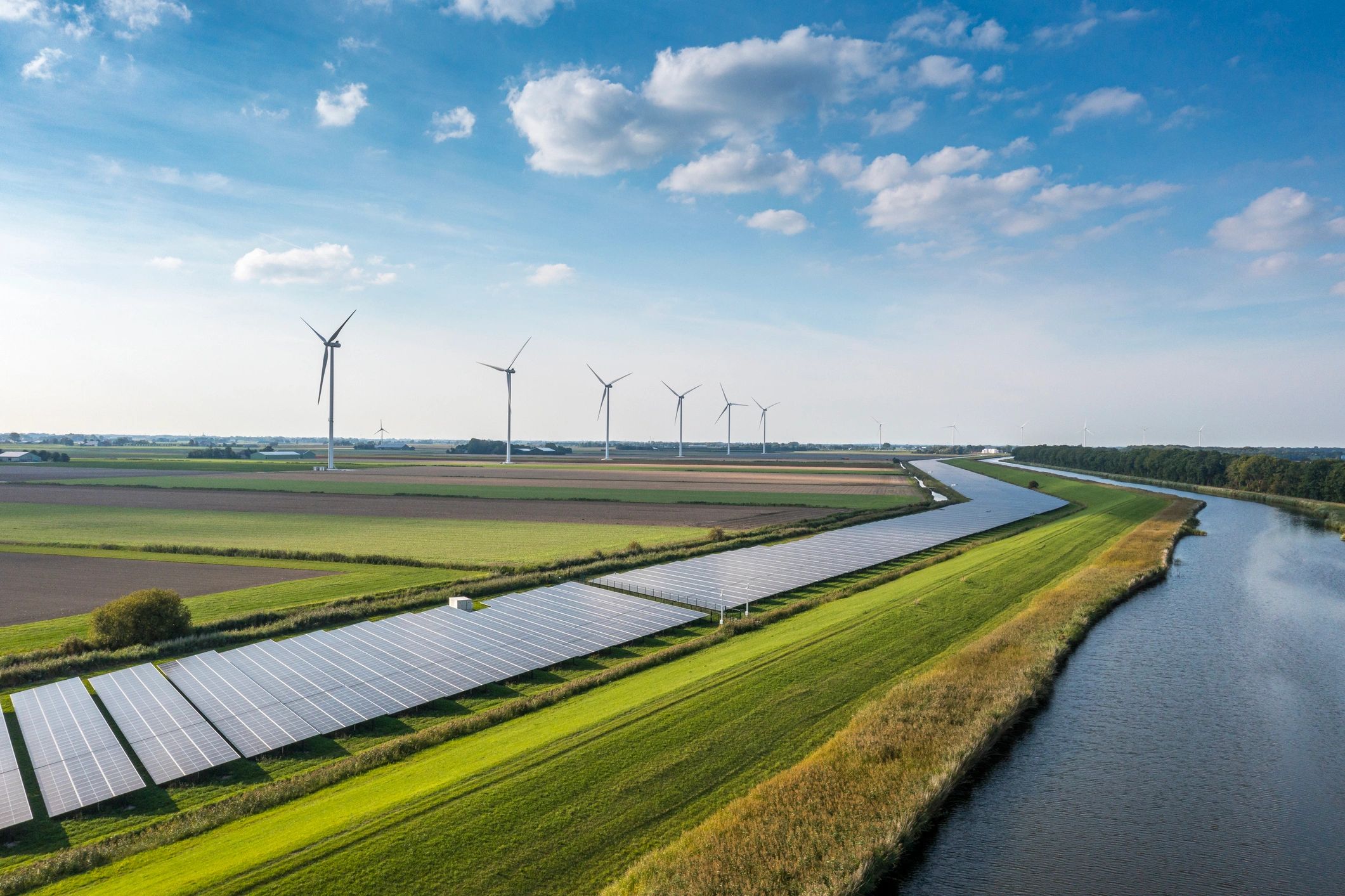 Wind turbines and solar panels in a green rural landscape under a blue sky.