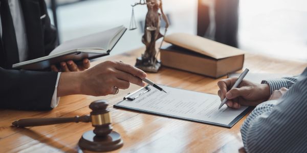 Two people reviewing legal documents with a gavel and law book on the table.