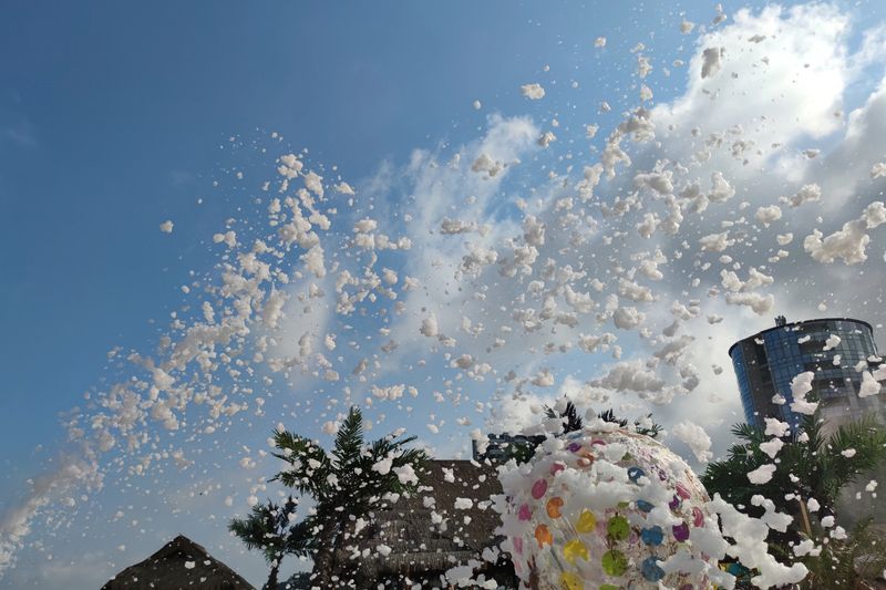 foam party on the beach, flying foam against the background of palm trees and a sunny sky.