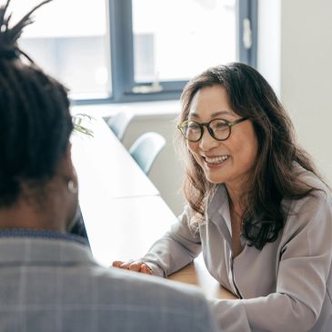 Two colleagues having a friendly conversation at a table in a bright office.