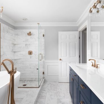 Modern bathroom with white marble, navy vanity, and brass fixtures.