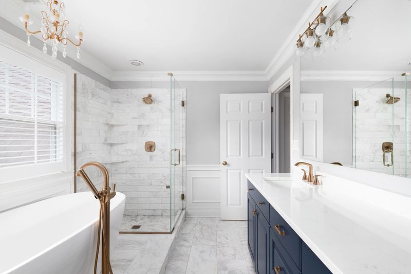 A beautiful bathroom with a blue vanity cabinet, standalone bathtub and shower, and gold faucets.