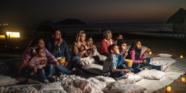 Family and friends enjoying an outdoor movie night on the beach at dusk.