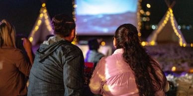 Couple watching an outdoor movie at night with festive lights.