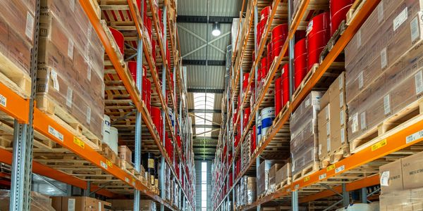 Warehouse aisle filled with pallets of red barrels and boxed goods.