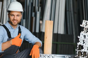 Smiling construction worker giving thumbs up in a warehouse.