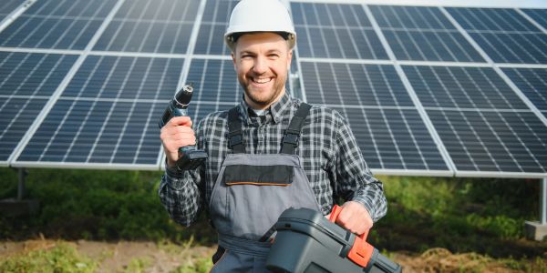 Technician smiling with tools in front of solar panels.