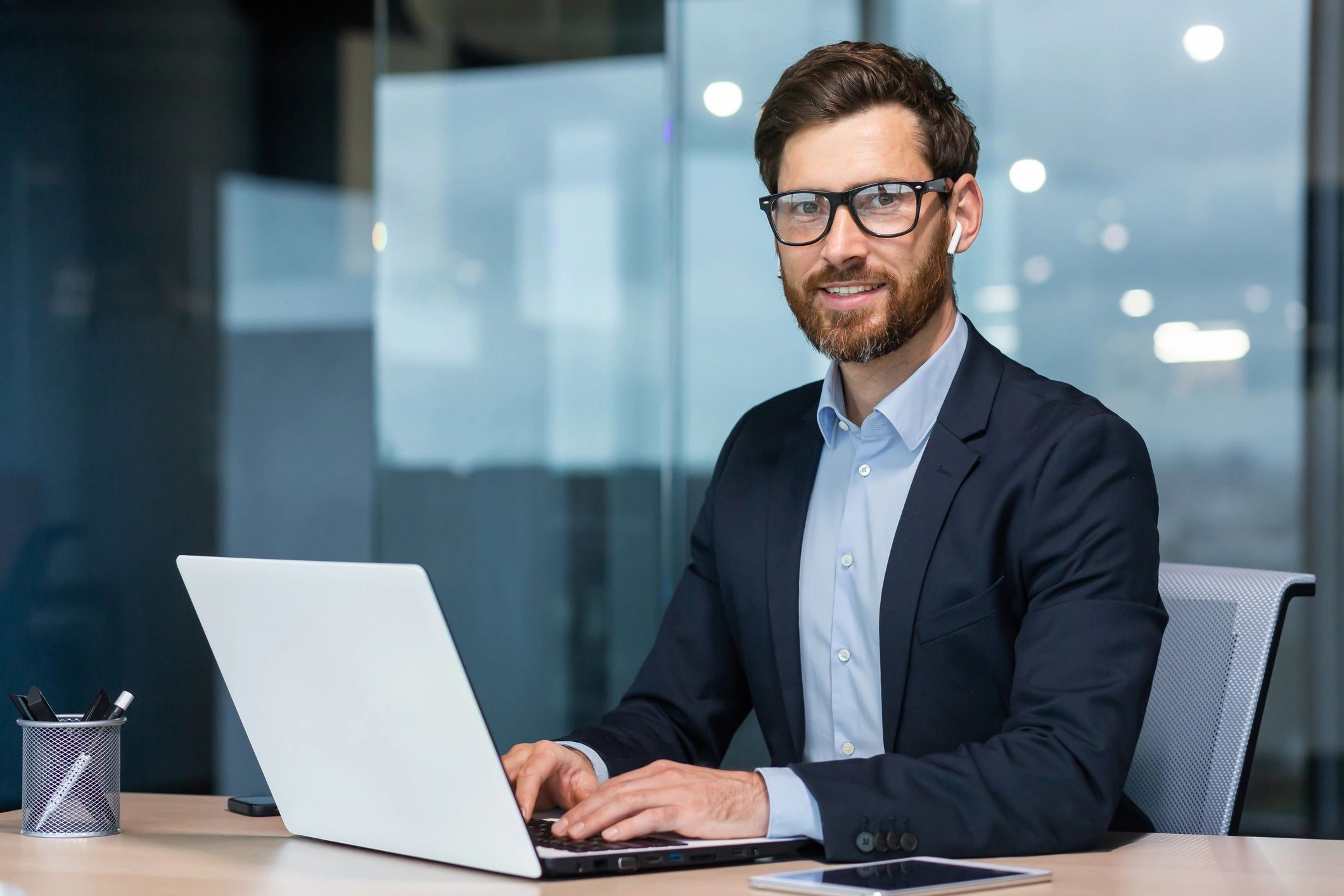 A man sitting at a desk with a laptop.  He is smiling with a look of anticipation.