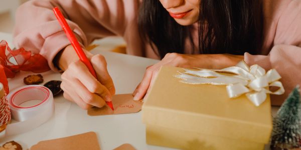 Person writing a gift tag next to a wrapped present.