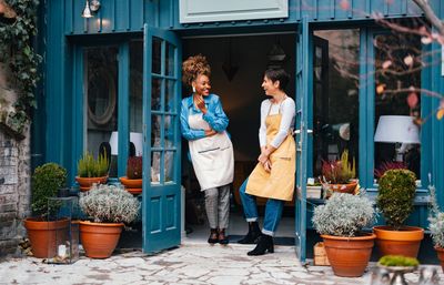 Two women chatting happily at the entrance of a charming blue shop.
