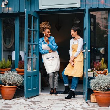 Two women chatting happily at the entrance of a charming blue shop.