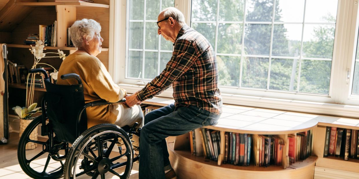 Elderly man holding hands with an elderly woman in a wheelchair.