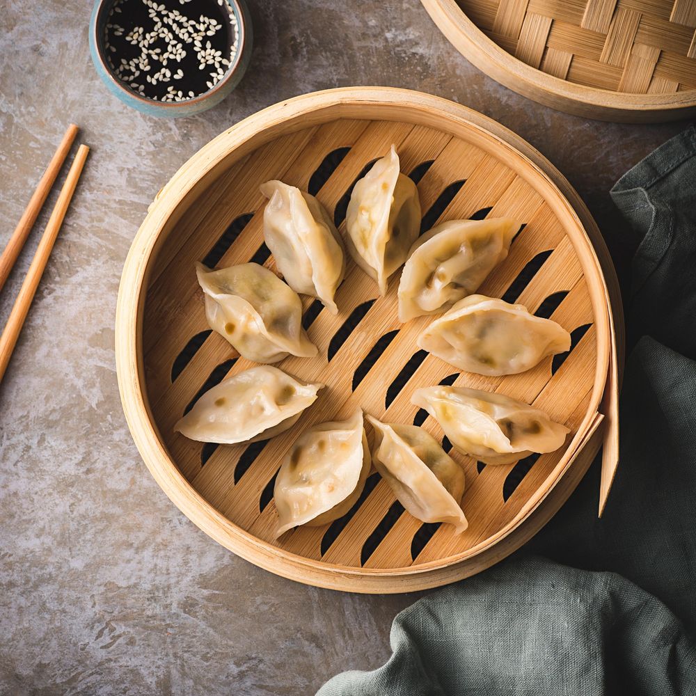 Steamed dumplings arranged in a bamboo steamer basket with soy sauce and chopsticks.