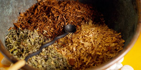 Three types of dried herbs or wood chips in a rustic bowl with a small spoon.