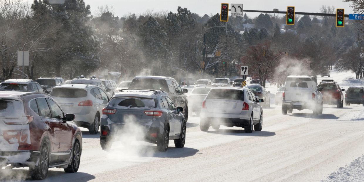Cars driving on a snowy road with visible exhaust in cold weather.