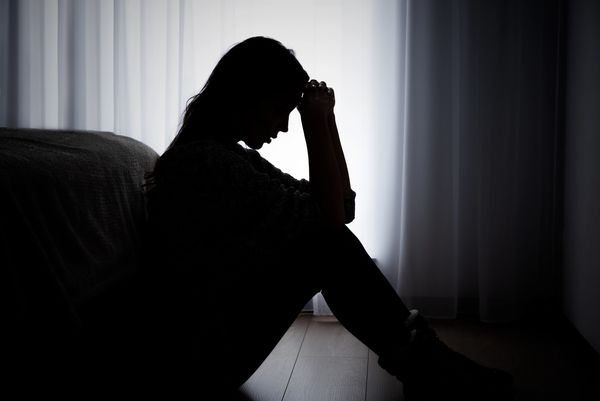 Silhouette of a person sitting with head in hands, appearing distressed.