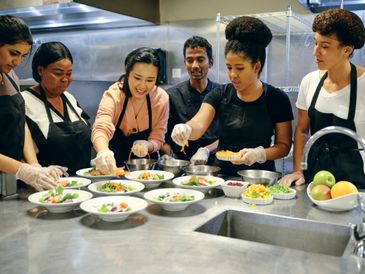 Diverse group preparing salads together in a kitchen.