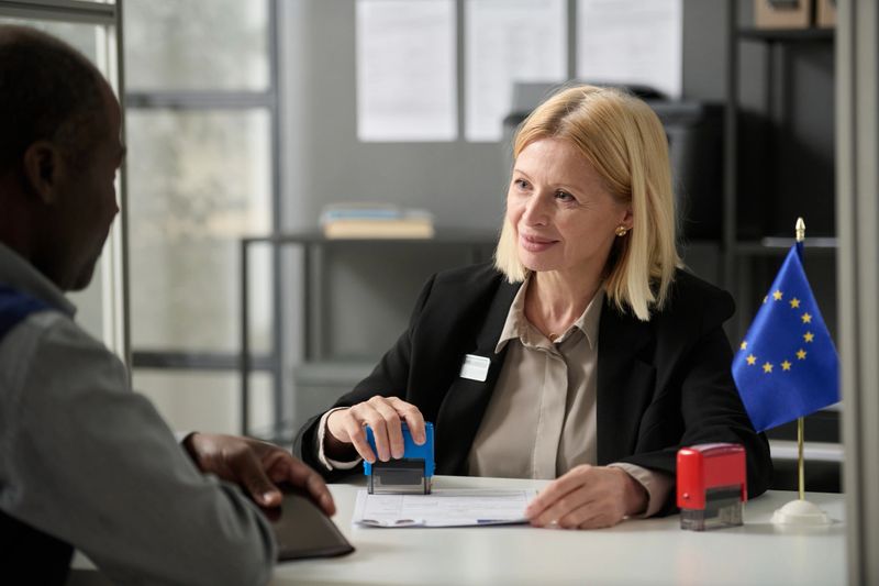 Portrait of smiling mature woman consulting person in EU immigration office or government agency and stamping forms