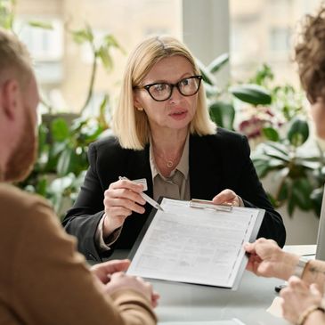 A professional woman explains a document to a couple in a bright office.