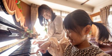Girl and woman playing piano together happily.