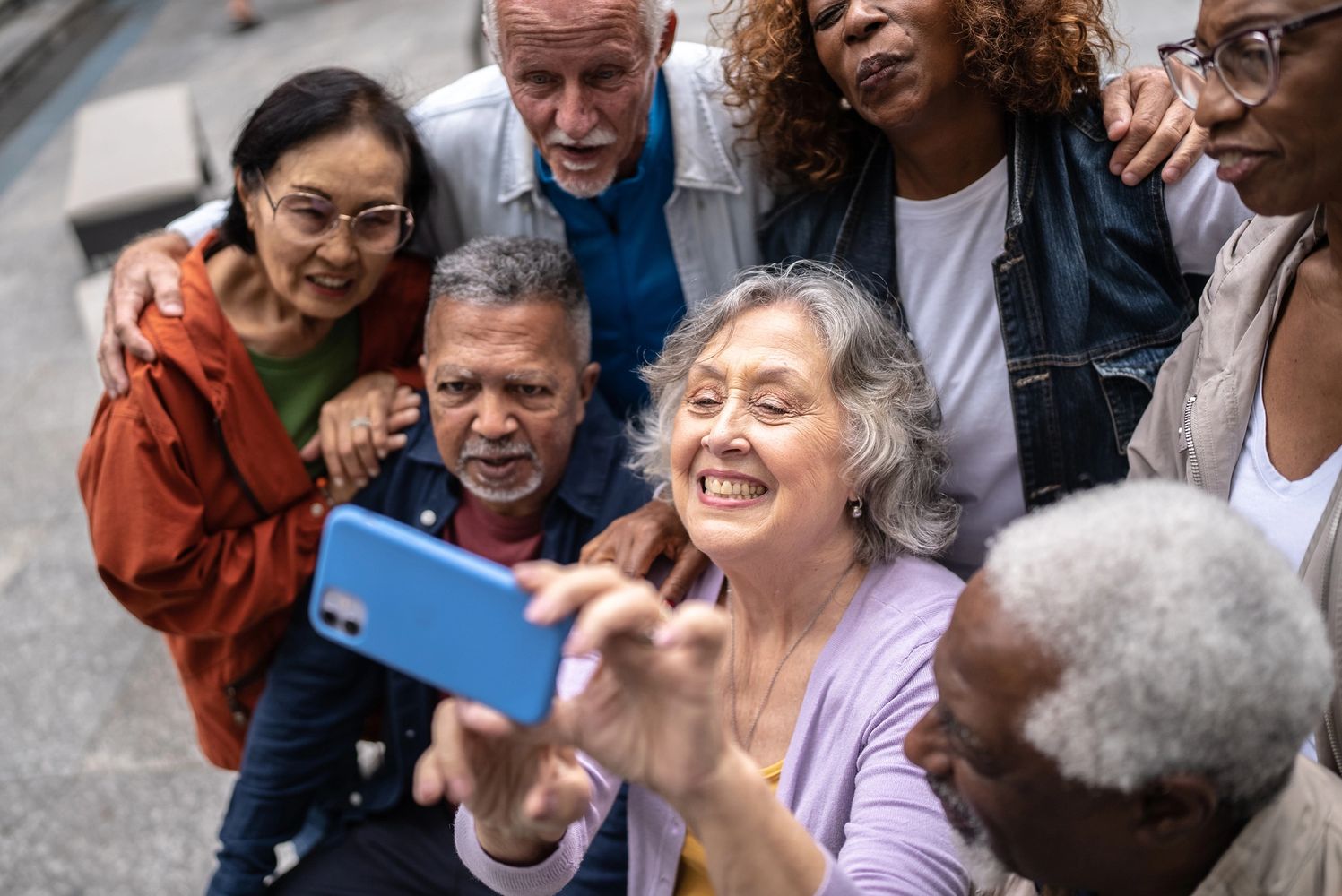 A diverse group of seniors happily taking a selfie together outdoors.