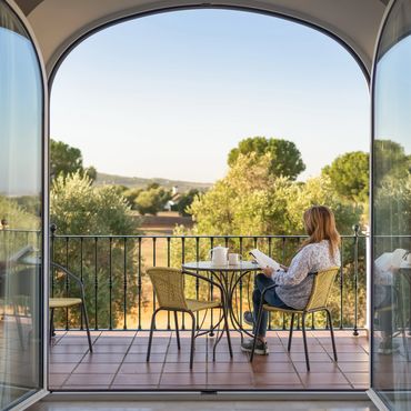 Woman reads on a balcony overlooking trees and hills in the morning.