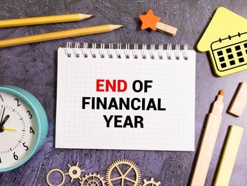 Notepad with 'END OF FINANCIAL YEAR' surrounded by office supplies and clock.