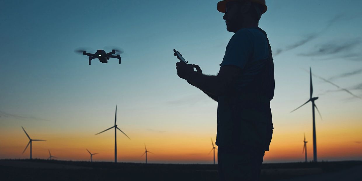 Person flying a drone near wind turbines at sunset.
