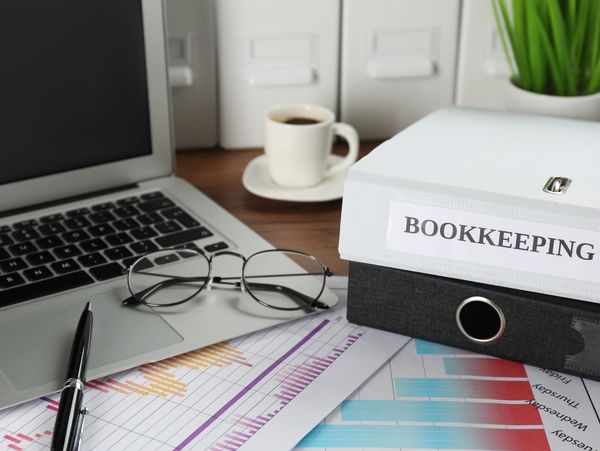 Office desk with bookkeeping files, laptop, glasses, and coffee cup.