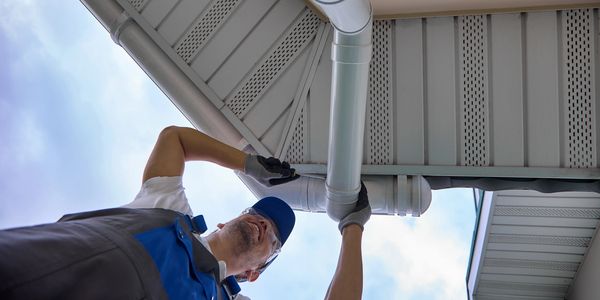 Worker inspecting a rain gutter on a house roof.