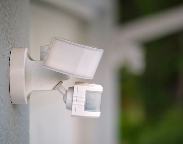 White motion sensor light mounted on a wall outdoors.