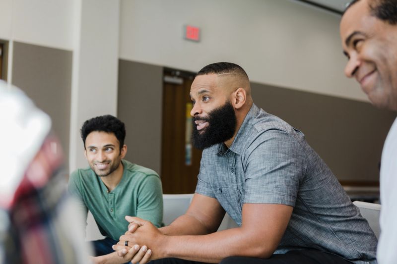 Three diverse men smile during group therapy.
