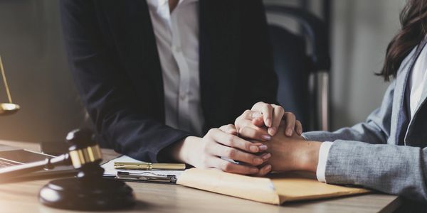 Two professionals in suits holding hands across a desk with legal symbols.
