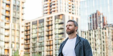 Man standing outside with urban buildings in the background.