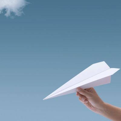 Hand holding a paper airplane in front of a clear sky.