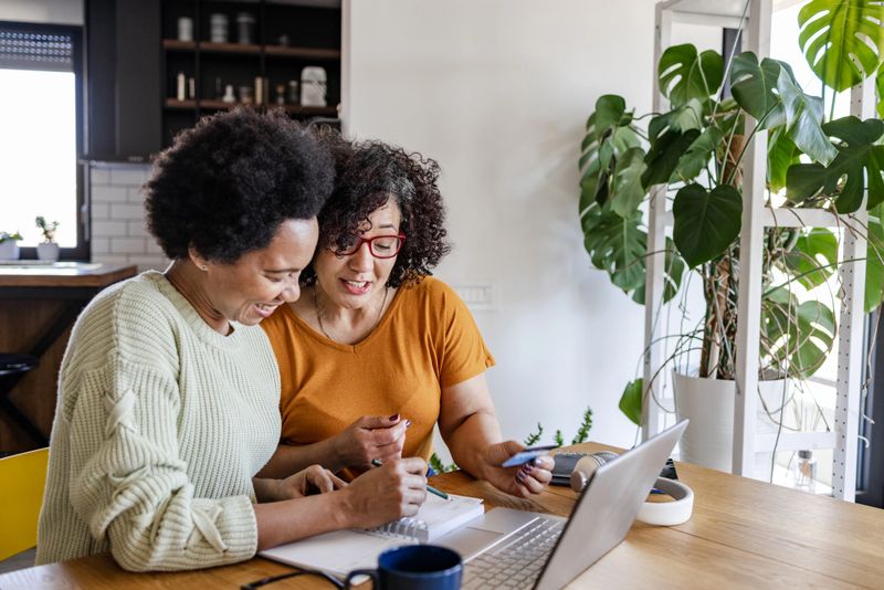 Gay couple sitting at the table in the kitchen and looking at the laptop. They are paying bills and making financial plans.