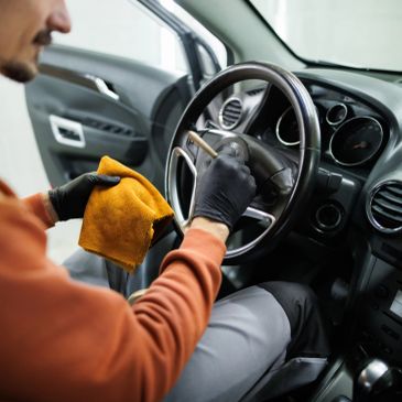Un homme nettoie le volant d'une voiture avec un chiffon jaune.