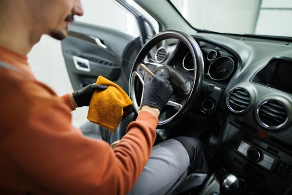 Person cleaning the steering wheel inside a car.