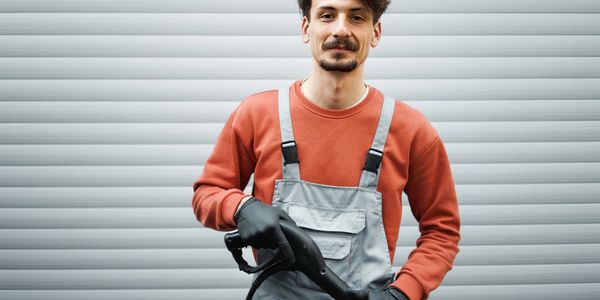 Man in work overalls posing with a tool.
