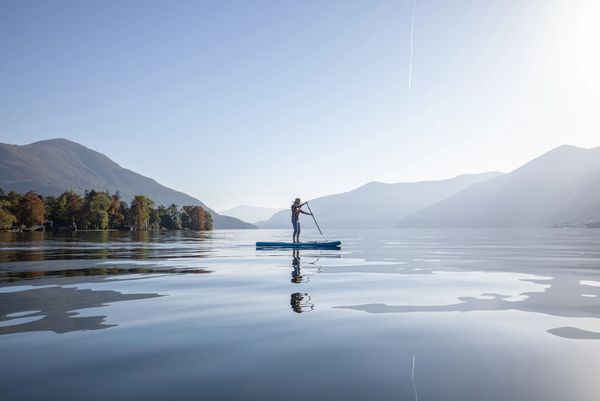 Person paddleboarding on a calm lake surrounded by mountains.